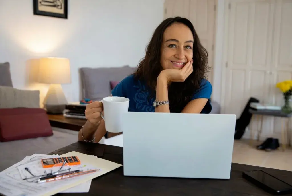 mujer sonriente sosteniendo taza mientras trabaja en una computadora