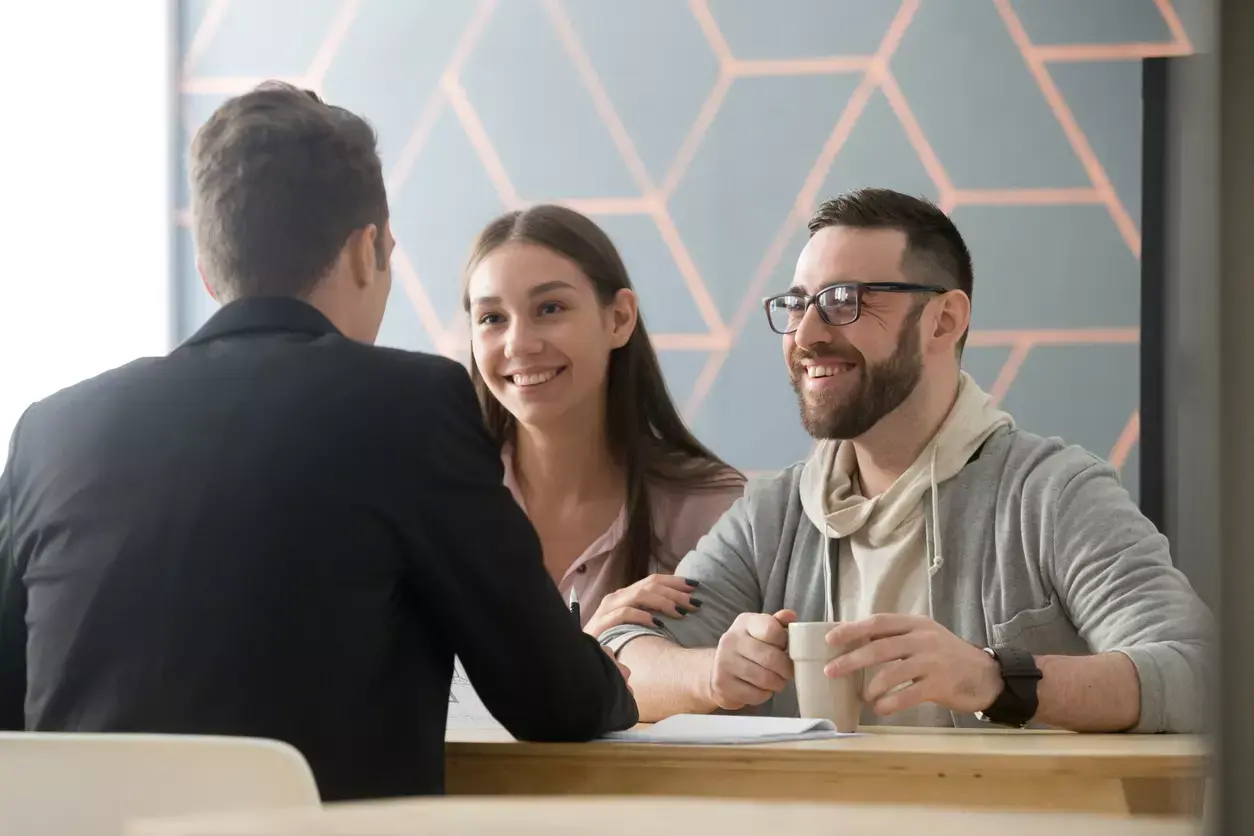 Entrepreneurs discussing a business loan with a cheerful advisor in a modern office setting.