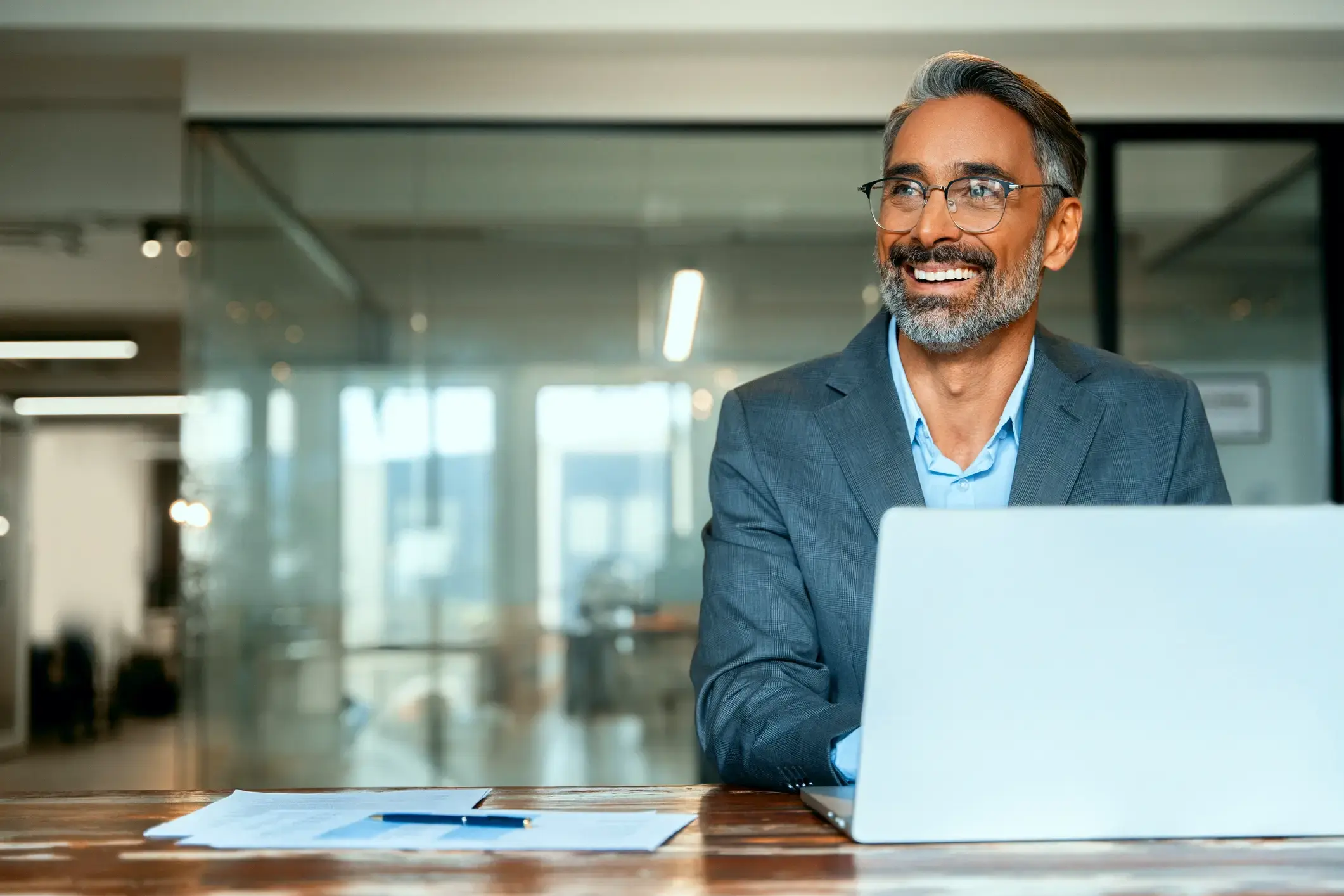 A smiling businessman at a laptop in a modern office, possibly reviewing successful loan options.